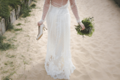 woman in wedding dress on the beach holding a bouquet and heels
